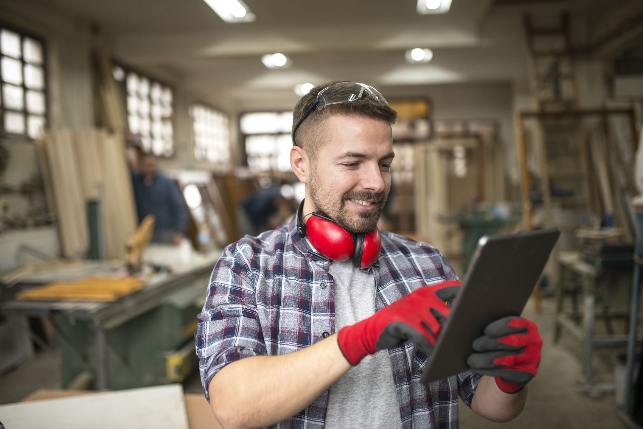 Portraet-des-laessigen-zimmermanns-mittleren-alters-mit-tablette-in-der-tischlerwerkstatt